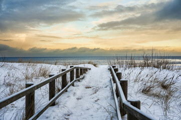 Snow-covered wooden boardwalk leading to Baltic Sea at sunset in Lilaste Latvia