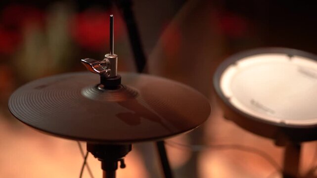 Close-up view of a drum set featuring a cymbal and electronic pad as a drummer strikes the cymbal with a stick, capturing the dynamic rhythm of the performance