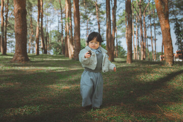 Adorable little Asian girl in a fleece jacket exploring a scenic pine forest while holding a pine cone for outdoor adventure and childhood travel concept © oatawa