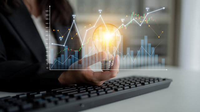 A business professional holds a light bulb over a keyboard while displaying graphs and data visualizations, symbolizing innovative ideas and strategic analytics in the workplace. Scalp - Powered by Adobe