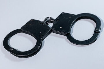 Black handcuffs resting on a white surface, showcasing the metallic texture and design, symbolizing...