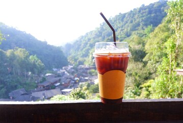 A cup of Iced Espresso on the wooden balcony with blurred a small village below,Maekumpong village in Chiangmai, Thailand 