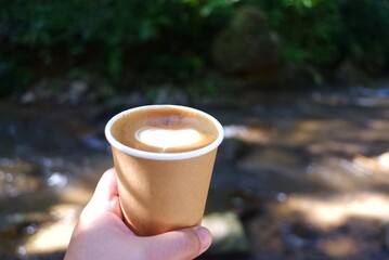 A woman hand holding a cup of hot latte with blurred a nature view