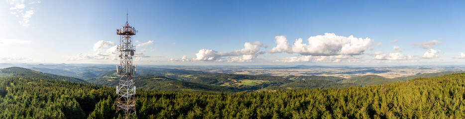 Rural summer landscape panorama of the G&oacute;ry Sowie (Owl Mountains), Poland, featuring rolling green hills, open meadows, dense forests, scattered farms, country roads, and a clear blue sky.