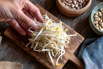 A hand selecting fresh bean sprouts on a rustic wooden board. Preparing healthy raw ingredients for cooking a vegetarian meal
