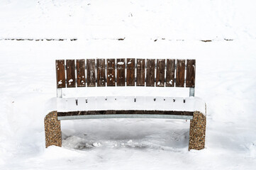 Park bench on a white snow and footpath in winter.