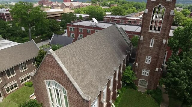 An elevated view captures the brick architecture and steep roofline of a university chapel surrounded by campus buildings and green trees.