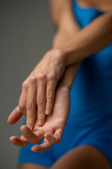 Fototapeta premium Close-up of athletic woman’s hands and forearms in blue sportswear, highlighting muscle tone, body control, and calm focus in a minimal studio setting.
