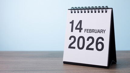Closeup studio photo of upright white desk calendar showing 14 February 2026, spiral bound, minimal typography, soft daylight, gray wood texture, clean background.