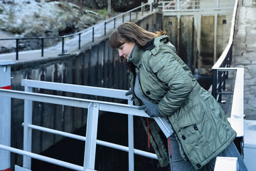 Slow pace lifestyle moment for adult woman leaning over a railing, observing water below during daily walk, expressing reflective thinking, independence and quiet connection to surroundings.