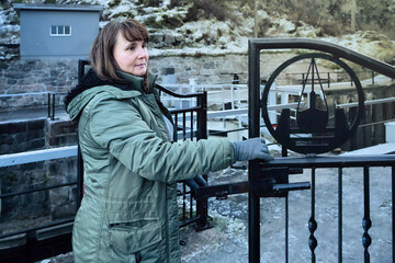 Quiet observation unfolds as an adult woman pauses by a gate near water, embracing slow living and active ageing through calm awareness during an unhurried outdoor walk.