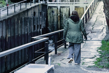 Steady movement continues as an adult woman walks along a stone path beside water, reflecting sustainable living and active ageing through a simple, self paced daily routine.