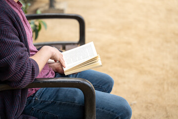 Person relaxing outdoors reading a book on a park bench, enjoying leisure time