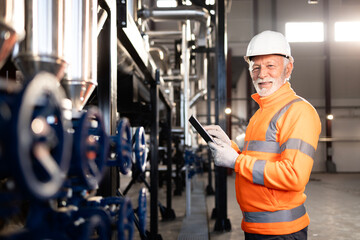 Senior engineer checking industrial machinery with tablet, smiling