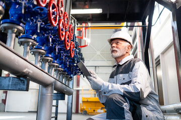 Engineer inspecting industrial plant pipes and valves with tablet