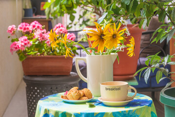 Summer breakfast in a patio. Mug of coffee, cookies, bouquet of yellow flowers on a table with tablecloth in a patio