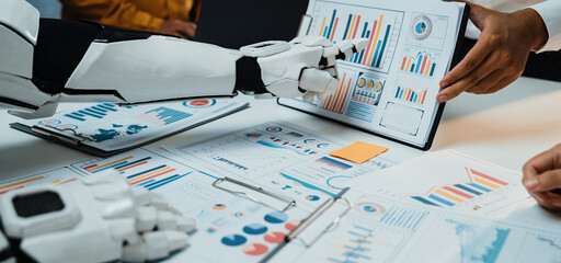 Explore the future of collaboration as a human and a robot analyze data together, surrounded by graphs and charts in a sleek office environment, showcasing innovation.Noogenesis