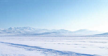 Snowy landscape, distant mountains under clear blue sky. Winter scene evokes cold, serene beauty. Flat terrain dominates foreground.
