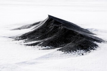 Black snowdrift isolated within a white snow landscape