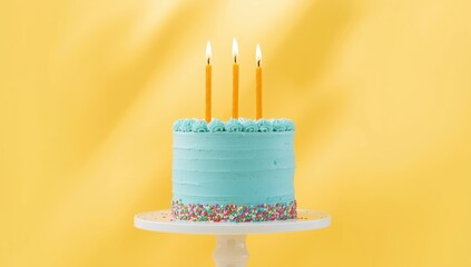 Celebratory blue birthday cake with three lit candles against a bright yellow backdrop, highlighting festivity