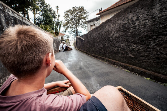 Scenic view of a child enjoying a thrilling toboggan ride downhill on a wicker sled in Funchal, Madeira, Portugal, with the famous Carreiros do Monte