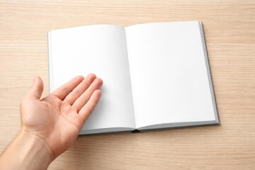 Obraz premium Hand open above a book mockup placed on a light wood grain surface