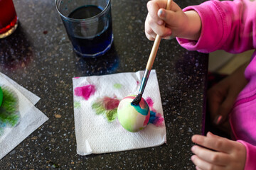 A childs hand, using a brush, paints an Easter egg on a paper towel, demonstrating the result of their creative endeavor.