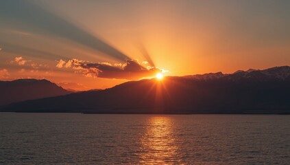 Evening scene of Baikal lake as the sun sets behind mountains casting rays, highlighting natural landscape and atmospheric lighting
