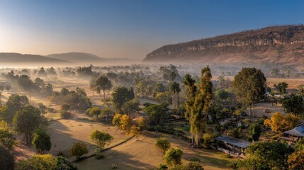 Verdant valley landscape shrouded in early morning mist beneath towering rock formation