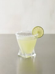 Classic margarita cocktail served in a salt-rimmed glass with a lime wedge on a neutral background. Copy space