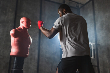 Fitness workout in gym. Strong African man fighter training punches with hitting punching bag mannequin. Kickboxer boxer man punching dummy. Training day in gym. Martial art kickboxing boxing fighting