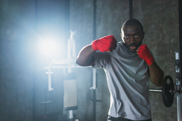 Workout in gym. African man fighter ready for fight punching with boxing wraps protective bandages to camera. Strong man training punches looking concentrated straight preparing for boxing sparring