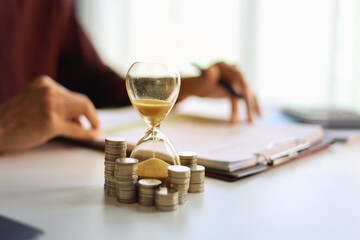 Coin stacks and sand clock on the table. Growing of income, saving or return investment through time. Time and money concept.