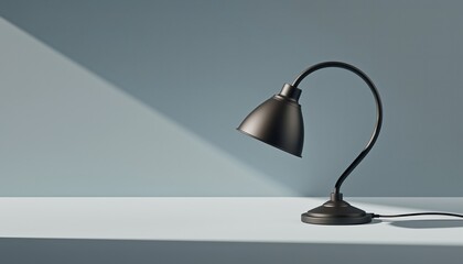 Black matte gooseneck desk lamp sits on a light grey table against a blue wall with a dramatic diagonal shadow, creating a minimalist and modern scene