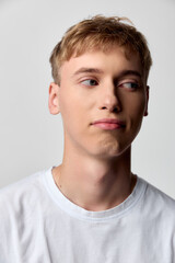Naklejka premium Young man in a white shirt with a thoughtful expression, studio lighting, looking away from the camera, conveying casual style, introspection, and calm mood.