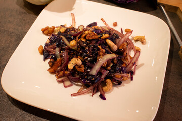 Pfannengericht aus Rothkohl, Wei&szlig;kohl, Walln&uuml;ssen, Erdn&uuml;ssen, cashewn&uuml;ssen und verschiedenen K&ouml;rnern, angerichtet auf einen wei&szlig;en Teller in Nahaufnahme