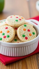 Colorful sugar cookies with sprinkles in a white baking dish on a wooden table with a red napkin