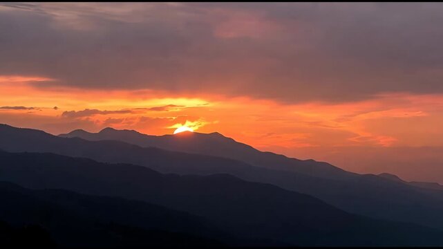 Majestic mountain range silhouette at vibrant sunset with glowing sun peeking over peaks and dramatic orange clouds painting the sky a breathtaking spectacle of natural beauty and serene twilight - Powered by Adobe