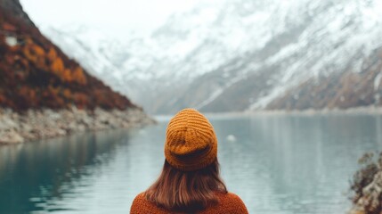 Woman standing by a lake with mountains in the background during a cloudy day
