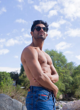 Hombre con el torso desnudo, jean azul y anteojos de sol en la monta&ntilde;a 