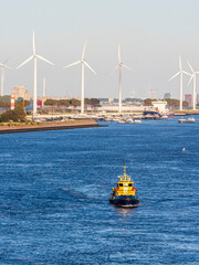 Tugboat sailing Nieuwe Waterweg past wind turbines in Maasvlakte