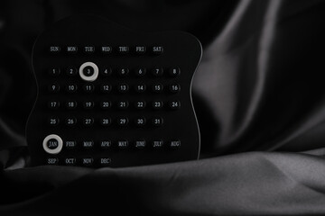 Black perpetual calendar with January 3rd highlighted, resting on dark draped fabric, creating soft and atmospheric composition.