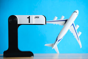Flip desk calendar showing January 1 with toy airplane on blue background, symbolizing travel plans and new beginnings.