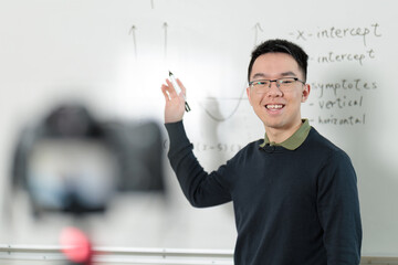 A happy Chinese mathematics instructor points to graphing concepts on a whiteboard while teaching an online lesson, perfect for online education, math tutoring, or STEM education concepts.