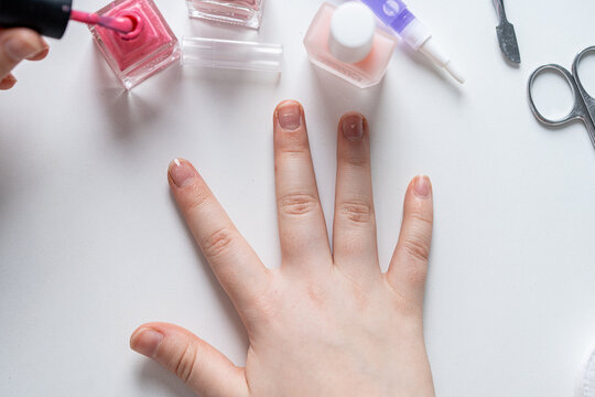 Baby manicure: Little girl's hand applying bright pink nail polish. A white background of a table on which manicure tools are placed.