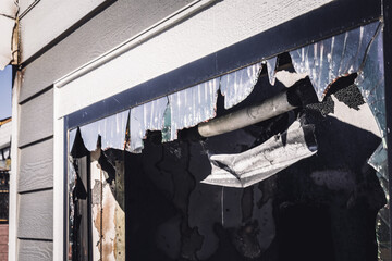 Damage to building exterior shows broken glass and charred surfaces after fire incident in a quiet neighborhood