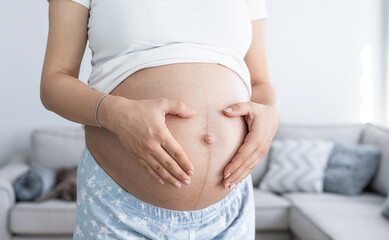 The pregnant woman makes a heart shape with her hand and holds it to her belly. Healty pregnancy concept.