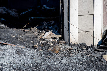 Fire damage aftermath shows charred debris and destruction near building exterior at a residential site