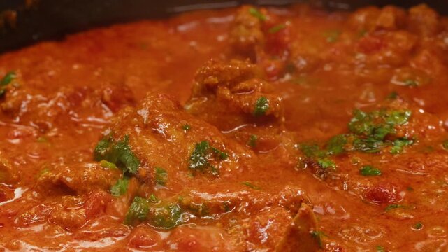 Cooking chicken Indian curry, tikka masala, chicken, lamb, mutton Rogan Josh grill boiling on pan, sauce. Dark background. Close up.