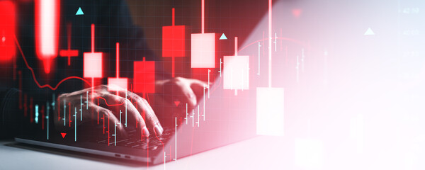 Hands typing on laptop with red candlestick chart overlay representing market crash and investment crisis in digital financial trading environment.